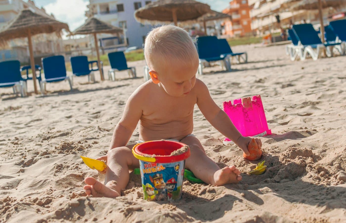 Topless boy holding blue plastic bucket on sand during daytime