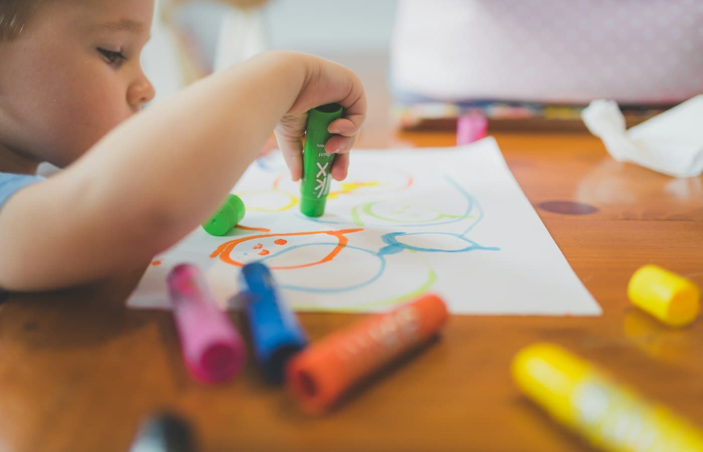 A little boy that is sitting at a table with some crayons