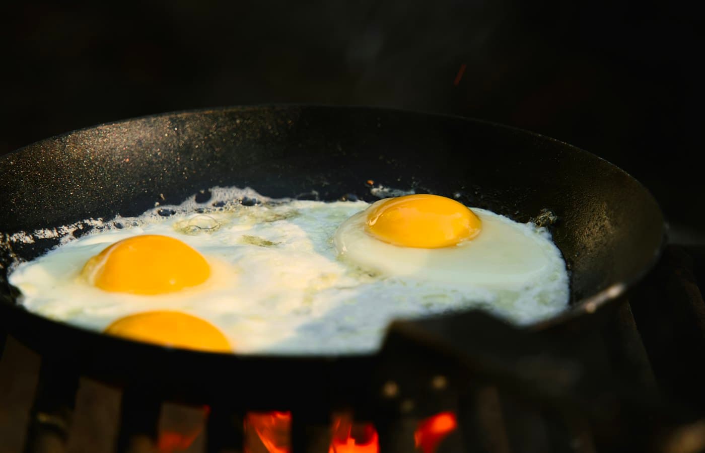 Three eggs frying in a black skillet over flames