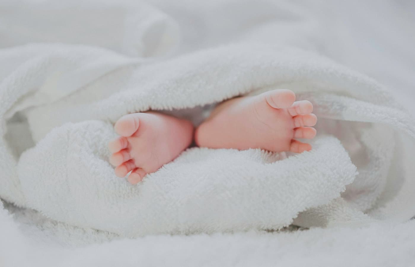 Barefooted baby covering white blanket