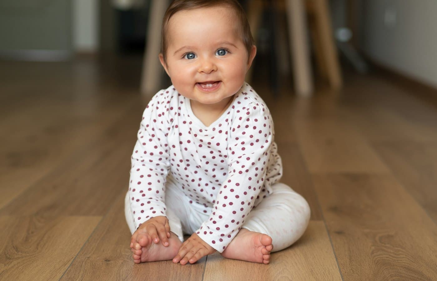 Baby in white and black polka dot onesie crawling on brown wooden floor