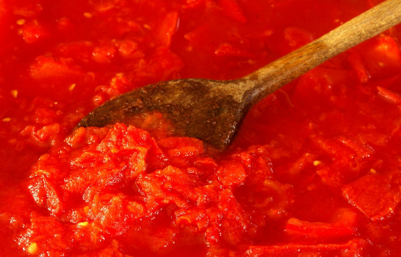 Tomato sauce being stirred with a wooden spoon