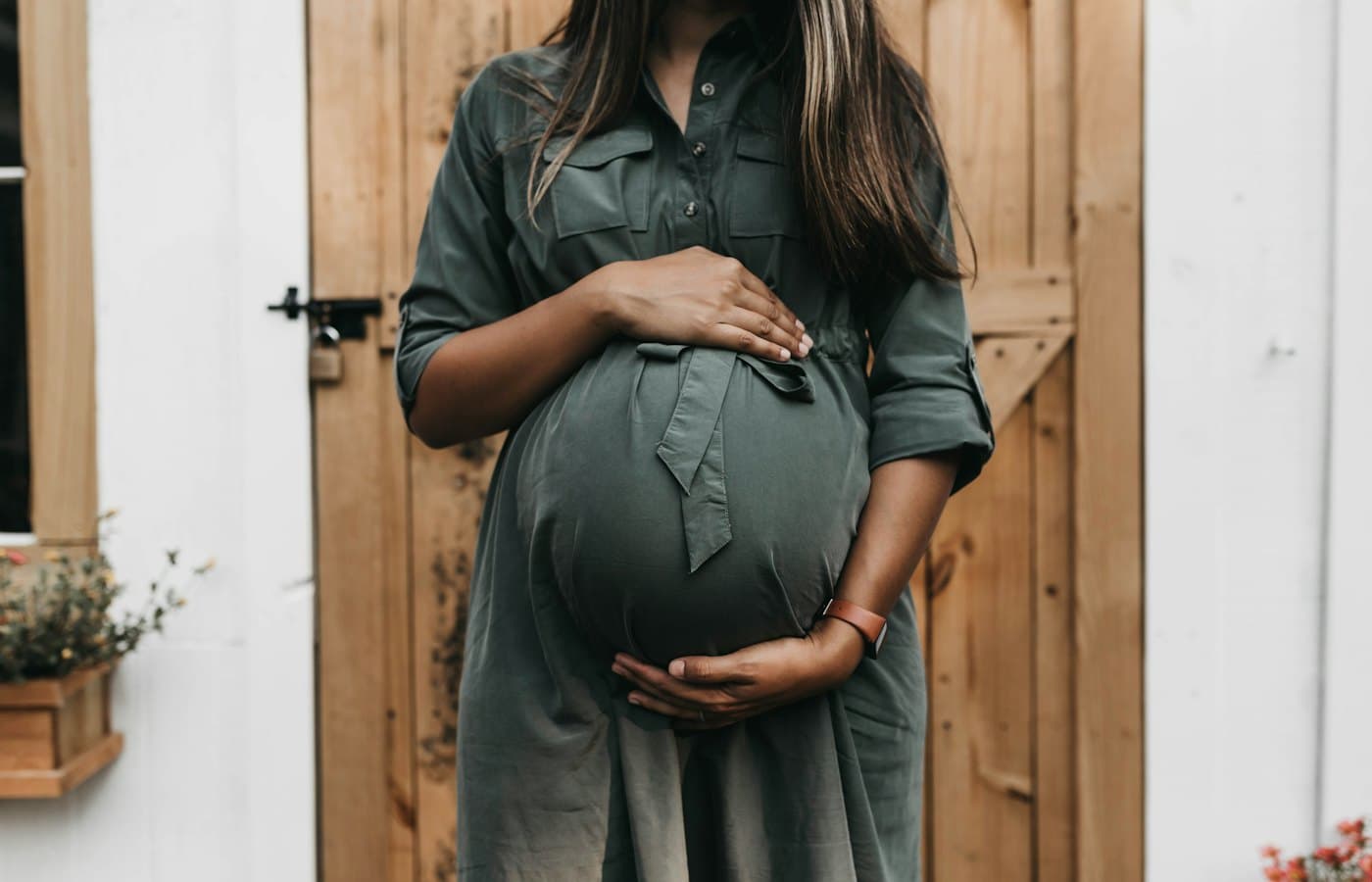 Pregnant woman holding belly before wooden door