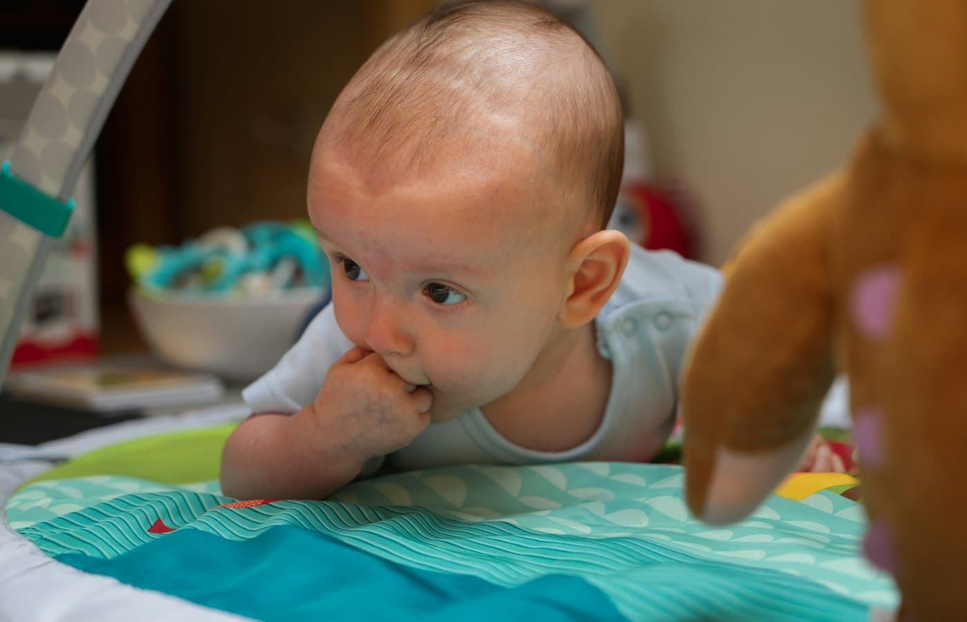 Baby in blue tank top on white and green bed