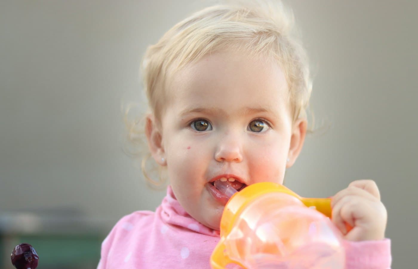 A little girl holding a plastic bottle in her mouth