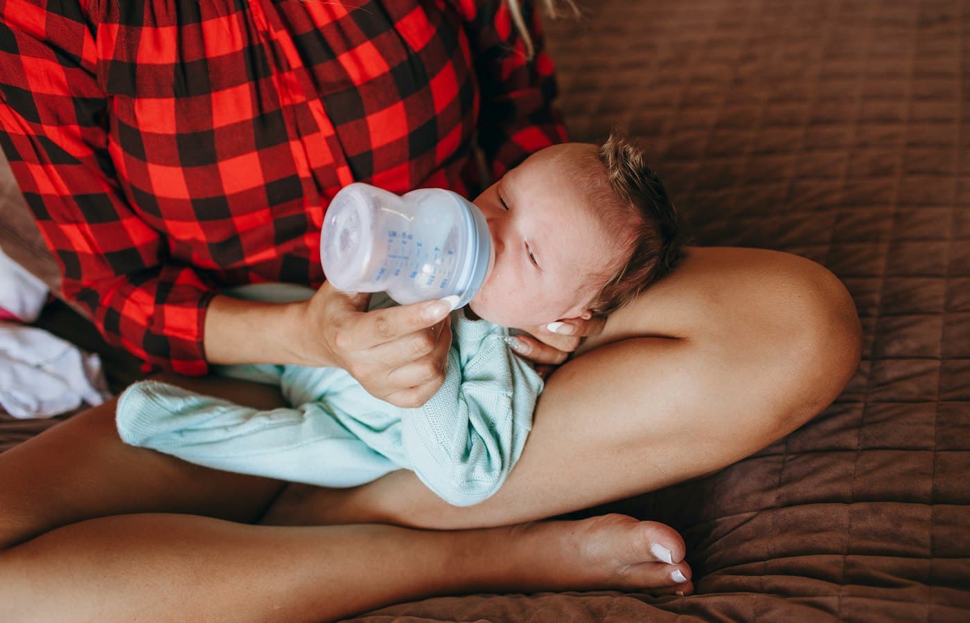 Woman in teal tank top drinking milk from feeding bottle
