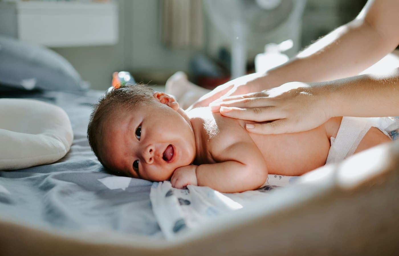 Baby laying on bed while woman massaging his back