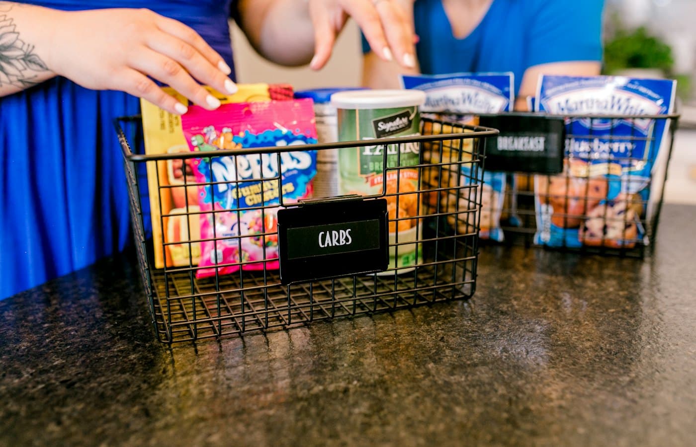 Hands organizing snacks into wire baskets on a countertop