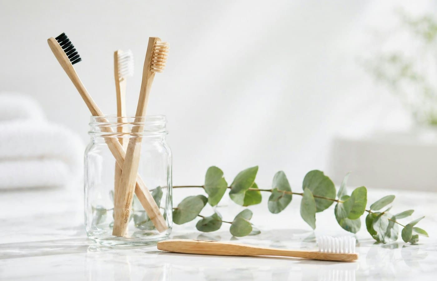 Bamboo toothbrushes in a glass jar with eucalyptus leaves