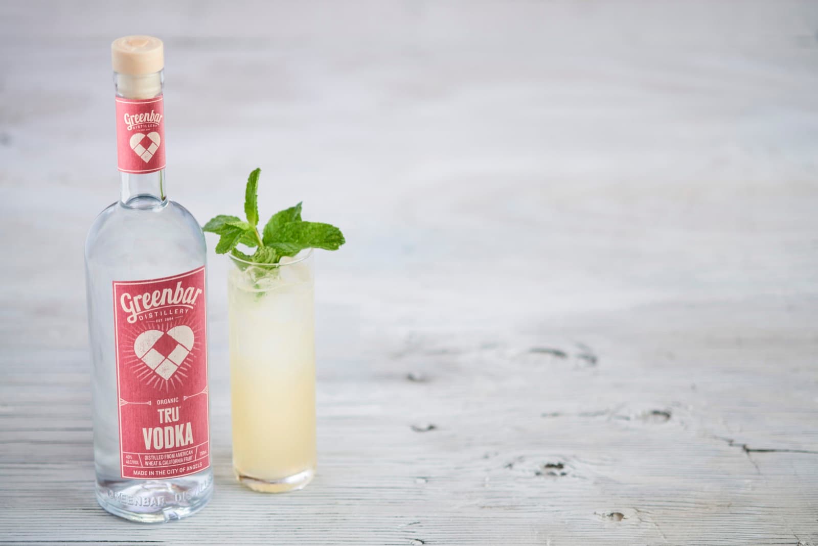 Bottle of Greenbar TRU Vodka beside a cocktail garnished with mint