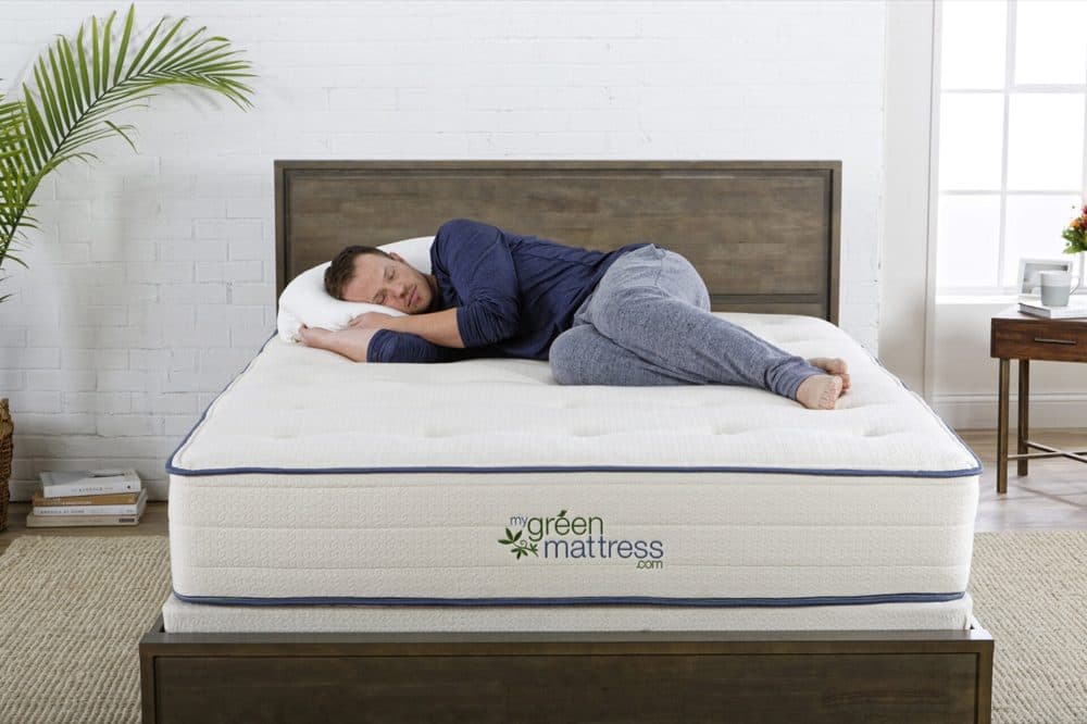 Man resting on a white tufted My Green Mattress mattress with blue piping in a bedroom