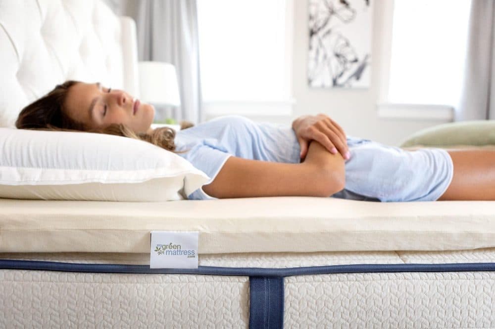 Woman lying on a cream latex topper with a My Green Mattress tag, placed on top of a mattress